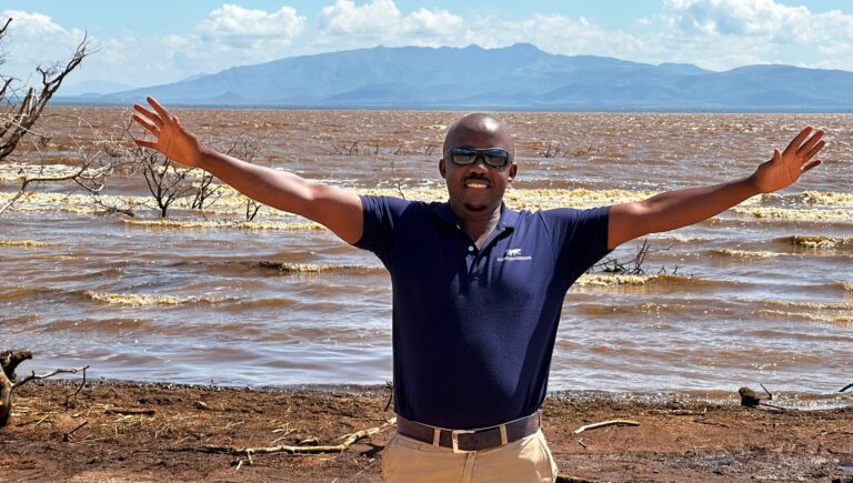 A man standing in front of a body of water with his arms out